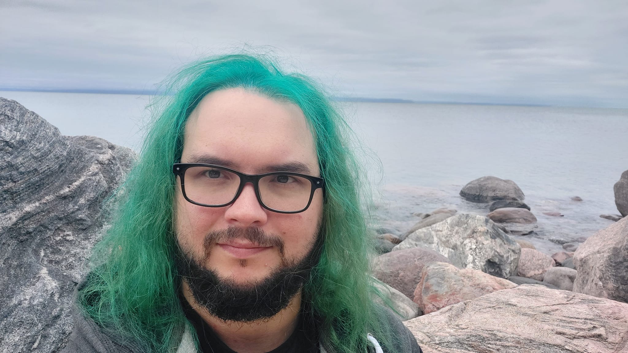 A man with green hair stands outside at a boulder breakwater, photo 12